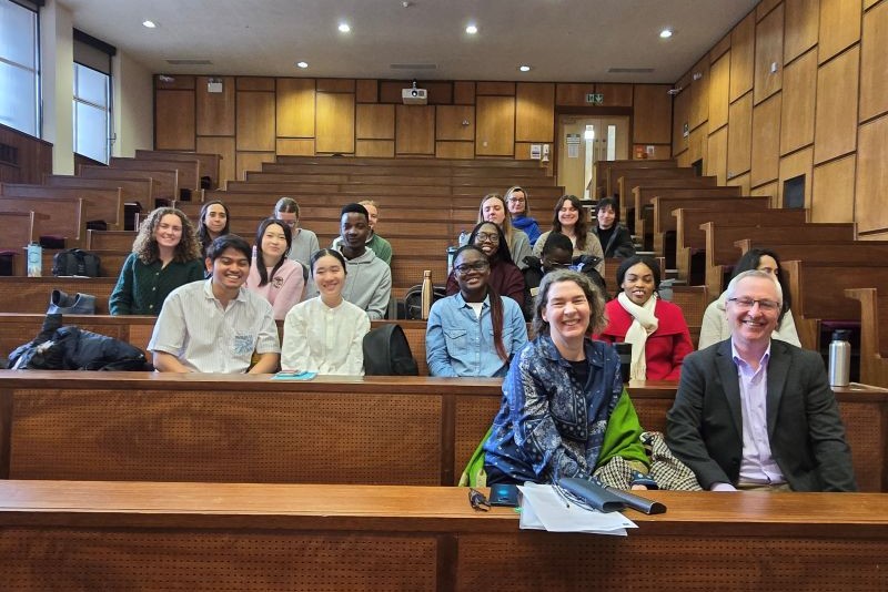several rows of visiting overseas students in lecture theatre with local hosts, a man and woman, in the front row